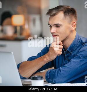 male freelancer works on a laptop in his kitchen. Stock Photo