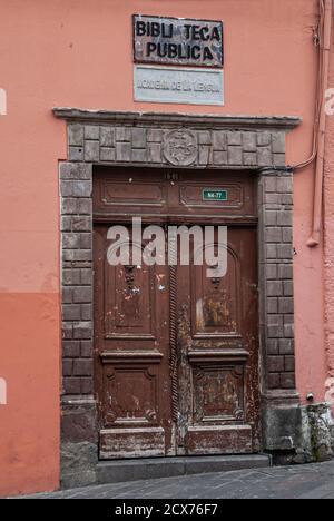 Quito, Ecuador - December 2, 2008: Historic downtown. Brown dilapidated sculpted door as entrance to Public Library, Maroon wall as backdrop. Stock Photo