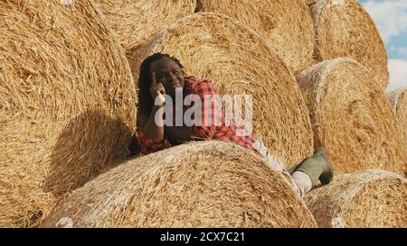 Young happy african farmer lying on the stack of hay rolls and resting. High quality photo Stock Photo