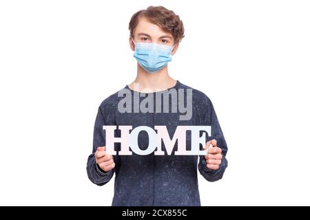 Coronavirus quarantine. Child wearing medical protective face mask, holds word Home - message for people to stay at home. COVID-19 - self isolation. Stock Photo