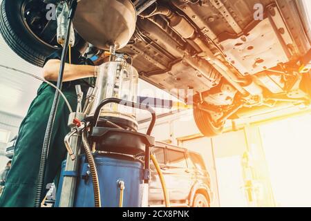 Worker drains oil from engine car during service in Auto Service Station in sunlight. Stock Photo