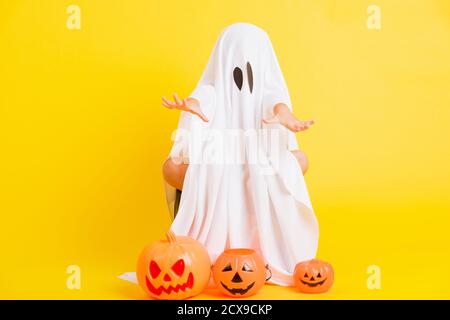 Funny Halloween Kid Concept, full body of a little cute child with white dressed costume halloween ghost scary he holding orange pumpkin ghost, studio Stock Photo