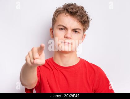 Portrait of happy teen boy pointing finger at camera, front view. Cute serious child in choose you, on gray background. Child in red t-shirt. Stock Photo