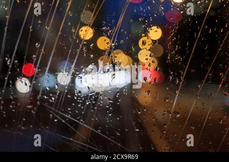 Selective focus at scratch and rain drops on glass of back of vehicle with blur night view with golden bokeh of street. Stock Photo