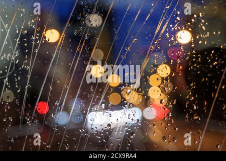 Selective focus at scratch and rain drops on glass of back of vehicle with blur night view with golden bokeh of street. Stock Photo