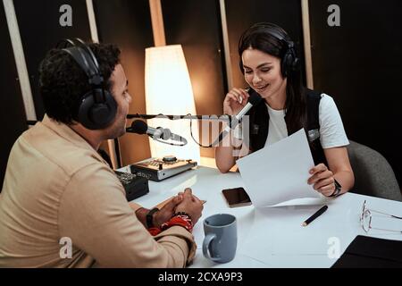 Portait of happy female radio host smiling, talking to male guest, presenter while moderating a live show in studio Stock Photo