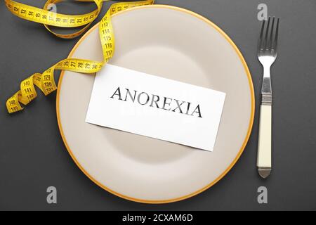 Plate with word ANOREXIA and measuring tape on dark background Stock Photo
