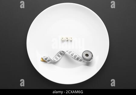 Plate with word EAT and measuring tape on dark background. Concept of anorexia Stock Photo