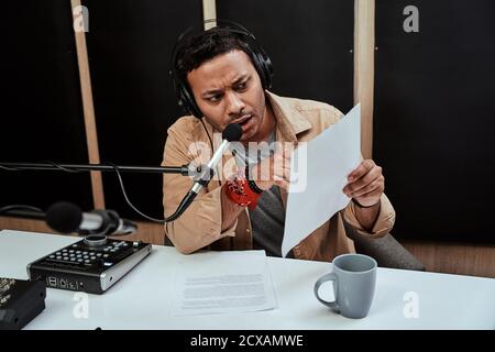 Portrait of young male radio host looking serious while reading a script paper, getting ready for moderating a live show in studio Stock Photo