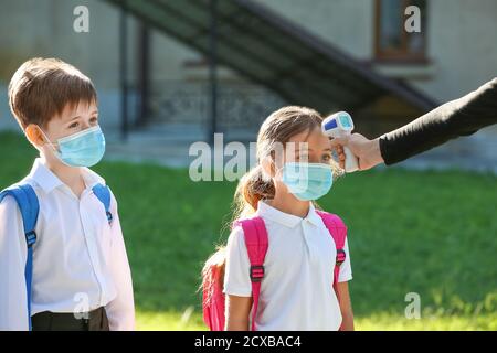 Teacher measuring temperature of pupils. Coronavirus epidemic Stock Photo