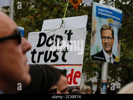 A protester holds up a placard reading 'don't trust Guido' as German Foreign Minister Guido Westerwelle next to an election campaign poster during the final election rally of the liberal Free Democratic Party FDP in Duesseldorf September 21, 2013. German voters will take to the polls in a general election on September 22. REUTERS/Wolfgang Rattay  (GERMANY - Tags: POLITICS ELECTIONS)