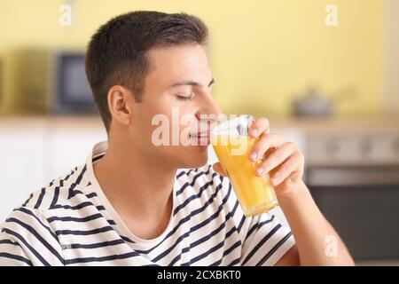 Handsome man drinking fresh orange juice in kitchen Stock Photo