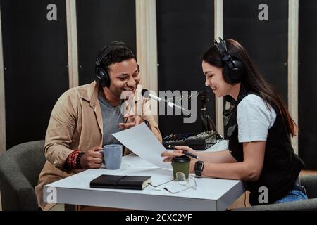 Portait of two radio hosts, man and woman talking with each other, reading a script while getting ready for a live show in studio Stock Photo