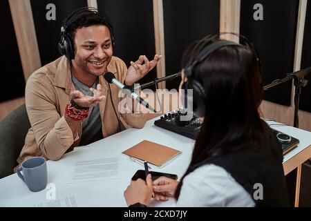 Portait of happy male radio host smiling, talking to female guest while moderating a live show in studio Stock Photo