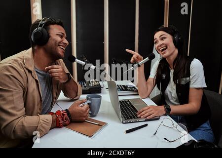 Portait of two happy radio hosts, young man and woman laughing while discussing various topics, moderating a live show in studio Stock Photo