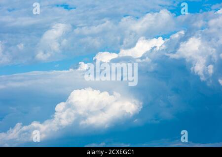 Large clouds and storm clouds close-up against a blue sky. White clouds are mixed with thunderclouds. Stock Photo