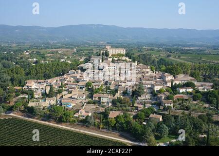 AERIAL VIEW. Medieval village with its castle at the top, overlooking the agricultural fields of the Durance Valley. Ansouis, Vaucluse, France. Stock Photo