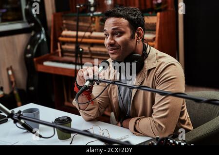 Portrait of young male radio host looking focused while speaking in microphone, moderating a live show Stock Photo