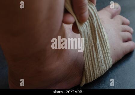 Middle-aged Caucasian man produces an independent bandage of his dislocated leg. He puts an elastic bandage over his swollen shin. First aid in sprain Stock Photo