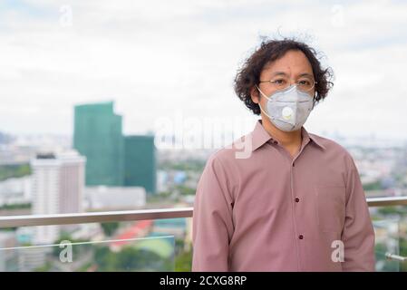 Portrait of Japanese businessman with curly hair wearing mask against view of the city Stock Photo