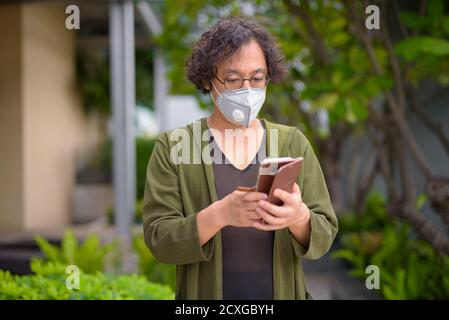 Japanese man with mask using phone in the rooftop garden Stock Photo