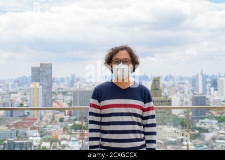 Japanese man with curly hair wearing mask against view of the city Stock Photo