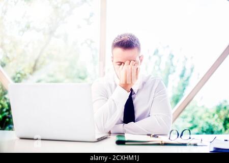 Cropped shot of stressed businessman with hand on his forehead sitting behind his laptop while having headache. Stock Photo