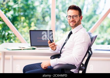 Shot of successful businessman sitting behind his laptop and text messaging while working in the office. Stock Photo