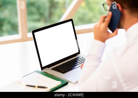 Rear view shot of businessman sitting behind his laptop and having a business call while workin in the office. Blank screeen. Stock Photo