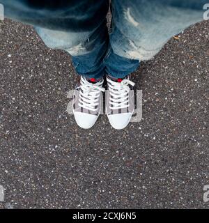 A young man's legs dressed in jeans and tennis on a background of asphalt. Photos with a small depth of field. Stock Photo