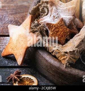 Homemade shortbread star shape sugar cookies with sugar and cinnamon powder in clay tray and sackcloth rag with cinnamon sticks on dark wooden backgro Stock Photo