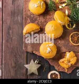 Whole and broken orange lemon homemade macaroons with white chocolate and citrus sugar and zest on old clay board over dark wooden background with Chr Stock Photo