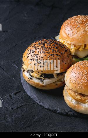 Three Homemade veggie burgers with sweet potato, black rice and red beans, served on stone round slate board over black textured background. Stock Photo