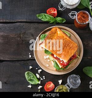 Low-carb gluten free Cloud bread veggie sandwich with spinach, avocado, feta cheese, tomatoes and pesto sauce, served on plate with jars of ingredient Stock Photo
