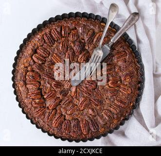 Homemade Big round caramel pecan pie in black iron forms, served with vintage cutlery on gray textile rag over white stone textured background. Flat l Stock Photo
