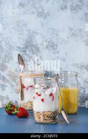 Healthy breakfast muesli, strawberries and yogurt with mango smoothie in glass mason jars. Served on blue wooden table with textured wall at backgroun Stock Photo