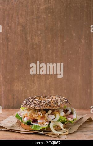 Whole Grain bagel with fried onion, green salad and prosciutto ham on paper over wooden textured background. With copy space Stock Photo