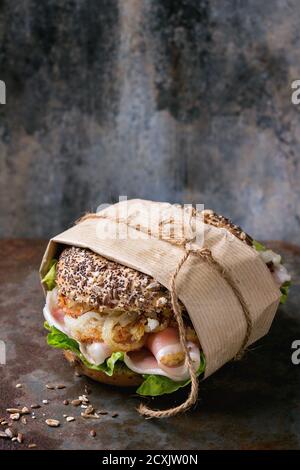 Papered Whole Grain bagel with fried onion, green salad and prosciutto ham over old rusty iron textured background. Stock Photo