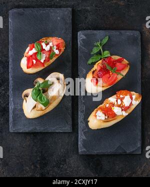 Various of mini bruschetta with tomatoes, strawberries, feta cheese, chicken, mushrooms and basil on toasted baguette, served on black slate board ove Stock Photo