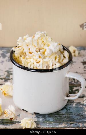 Prepared salted popcorn served in vintage white enameled mug over old white wooden background. With space for text. Stock Photo