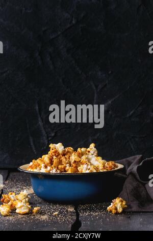 Caramelized sweet popcorn served in vintage enameled bowl with brown sugar and textile napkin over dark wooden background. Stock Photo