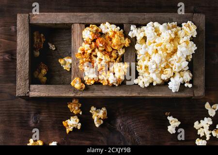Prepared salted and caramelized sweet popcorn in old wood three sectioned box over dark textured wooden background. Top view. With space for text Stock Photo