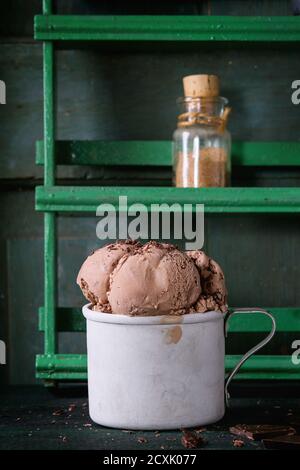 Frozen vintage aluminum mug with chocolate ice cream balls, served with chopped dark chocolate on old wooden table and rack with spices at background. Stock Photo