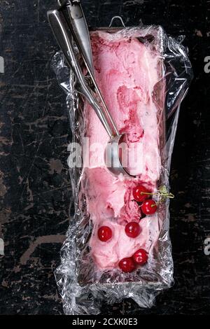 Homemade cherry sorbet in vintage iron container with polyethylene film, fresh cherry berries and metal spoon for ice cream over old black wooden text Stock Photo