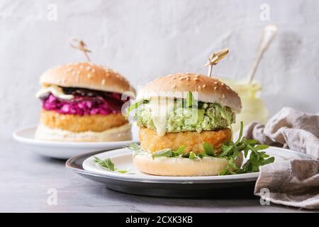 Two vegetarian hamburgers with onion and cheese cutlets, avocado salad, arugula, fried beetroot and yogurt sauce in white plate over gray texture back Stock Photo