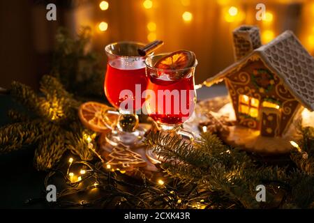 Christmas drink with spicy and berries. Cozy still Life with glasses, gingerbread house and spruce branches. Stock Photo