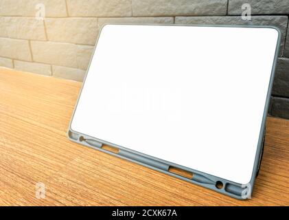 Blank space or empty space of tablet screen, white colour. Tablet on wooden desk, standing by its cover protection, grey colour brick wall background, Stock Photo