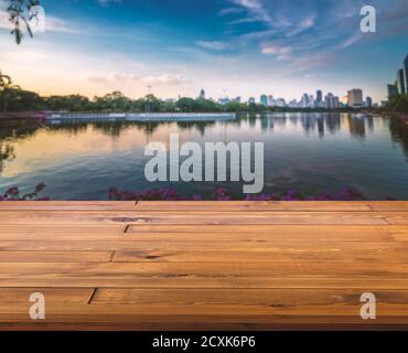 Beautiful plank wooden table, perspective view, empty space for product display. Blurred background sunset of lake in park and cityscape of Bangkok, T Stock Photo