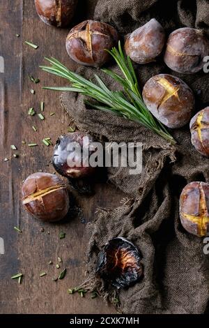 Roasted chestnuts in the ashes with rosemary on sackcloth over old dark wooden background. Top view with space for text. Stock Photo