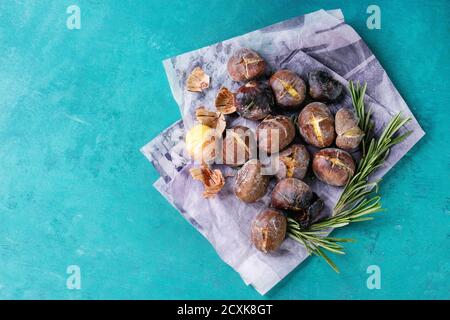 Roasted chestnuts in the ashes with rosemary on paper over bright turquoise wooden background. Top view with space for text. Stock Photo